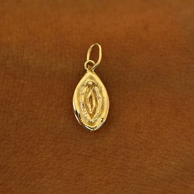 A solid 14k yellow gold Vulva Charm resting on the back of a model's hand