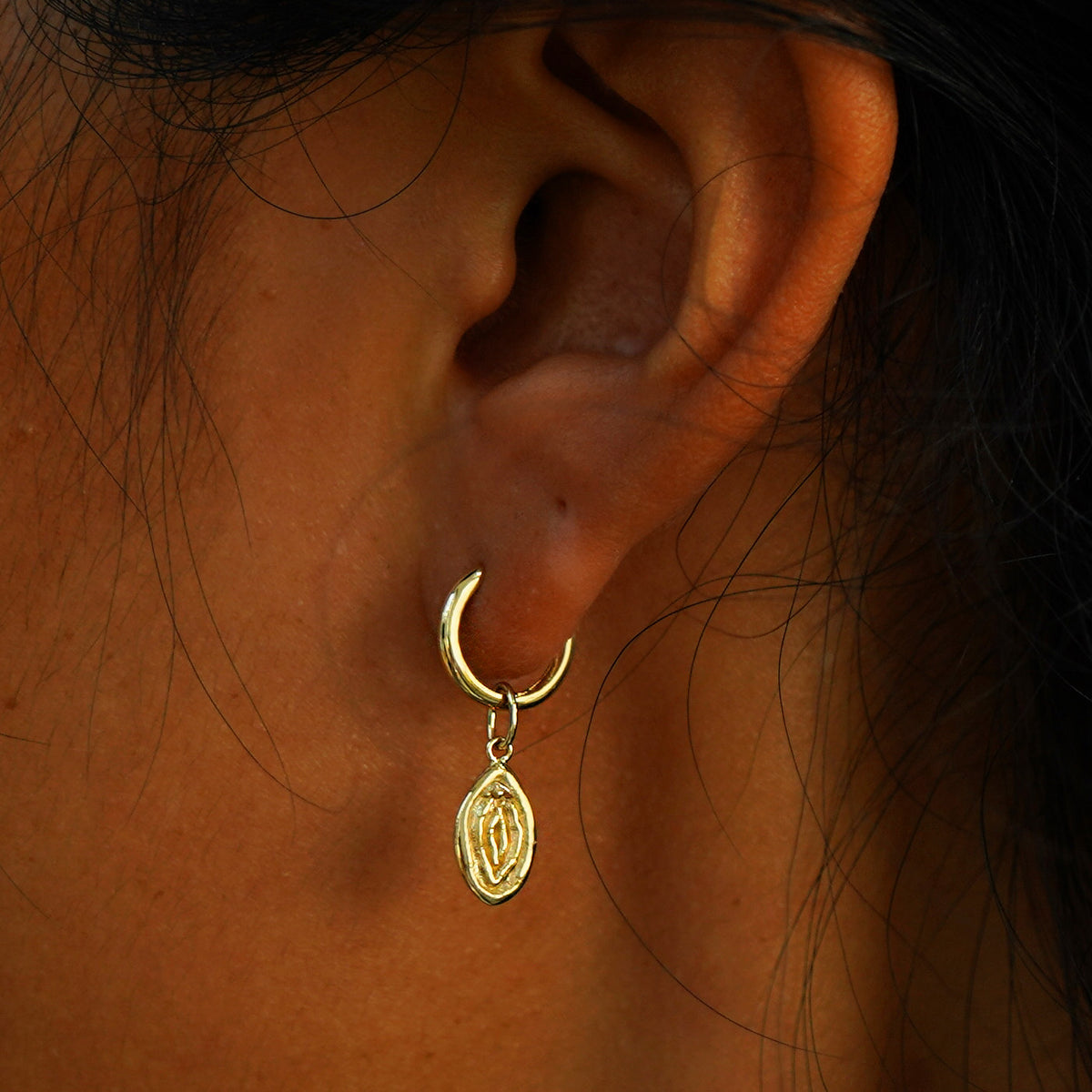 A model's ear wearing a yellow gold Vulva Charm on a Curvy Huggie Hoop