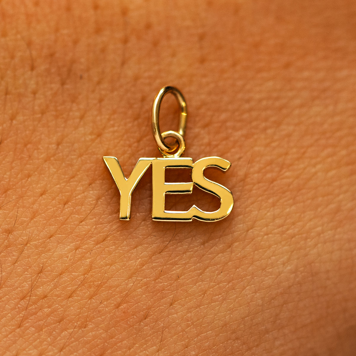 A solid 14k yellow gold Yes Charm on the back of a models hand