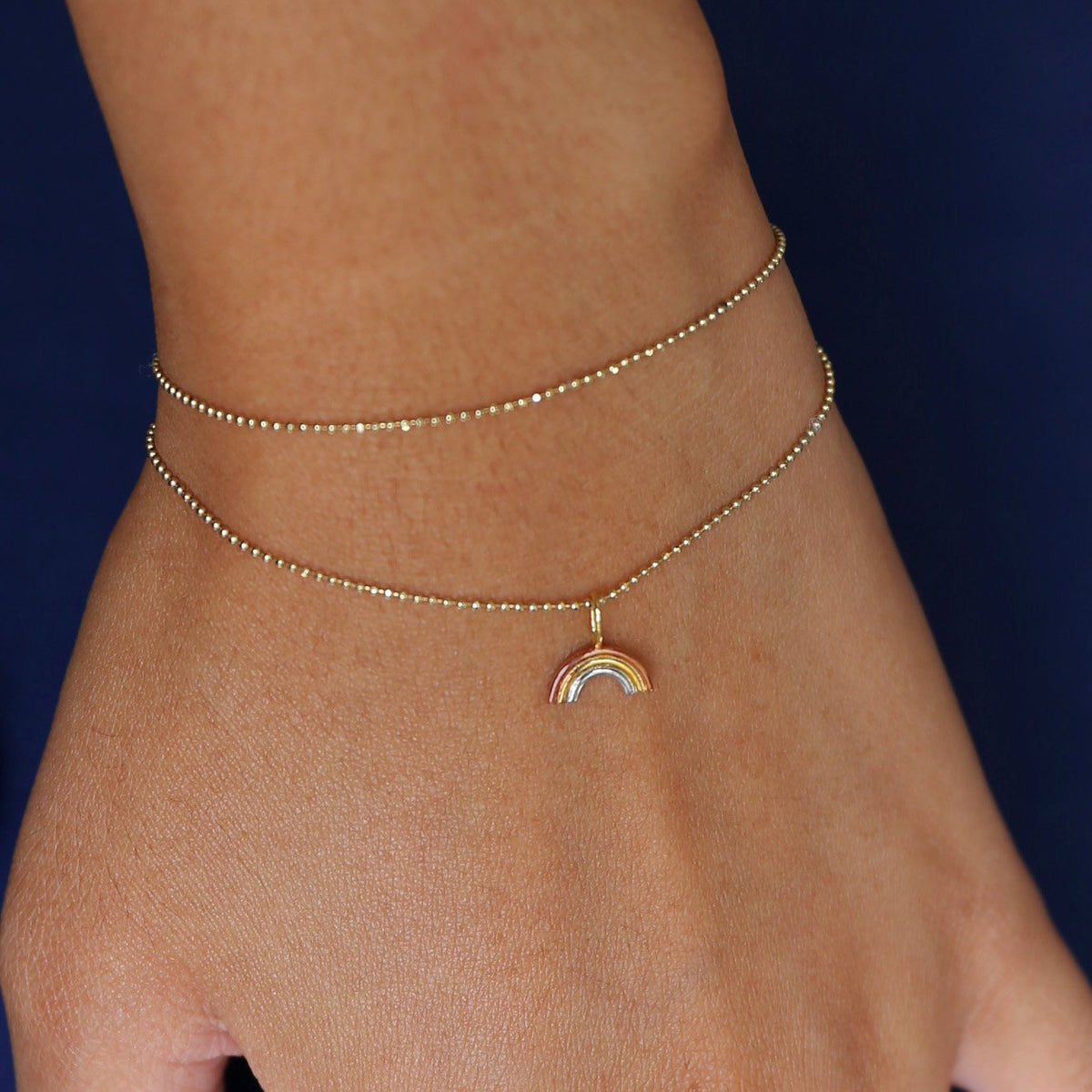 Close up view of a model's wrist wearing a Rainbow Charm on a yellow gold Bead Chain worn as a double wrapped bracelet