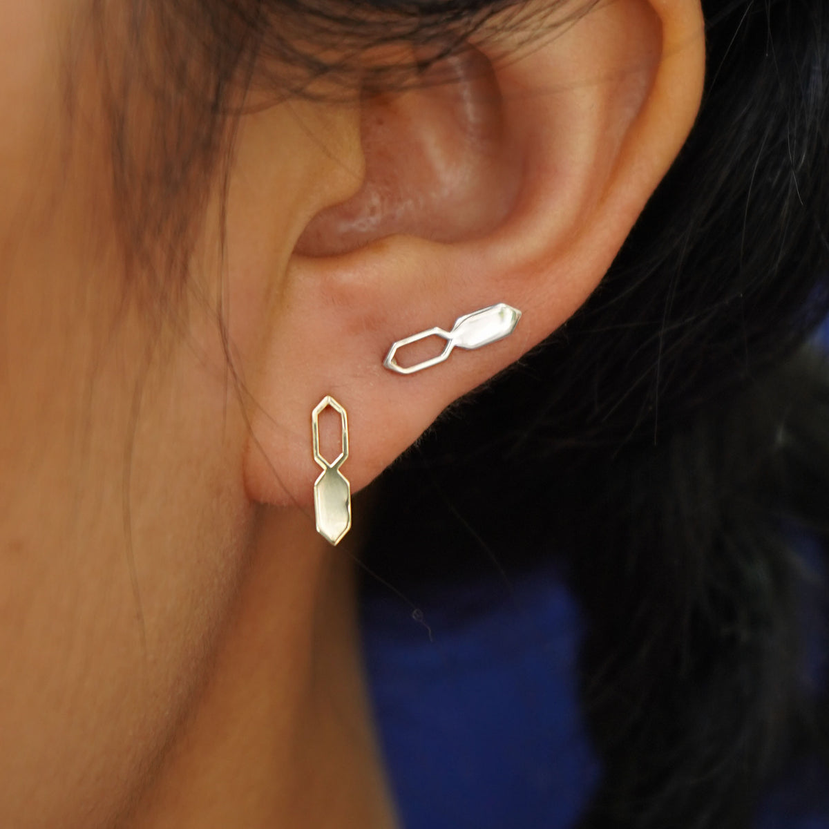 Close up view of a model's ear wearing two yellow gold Tanlah Earrings in two separate lobe piercings
