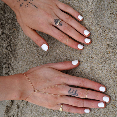 A model with their hands in the sand at the beach wearing various Automic Gold jewelry