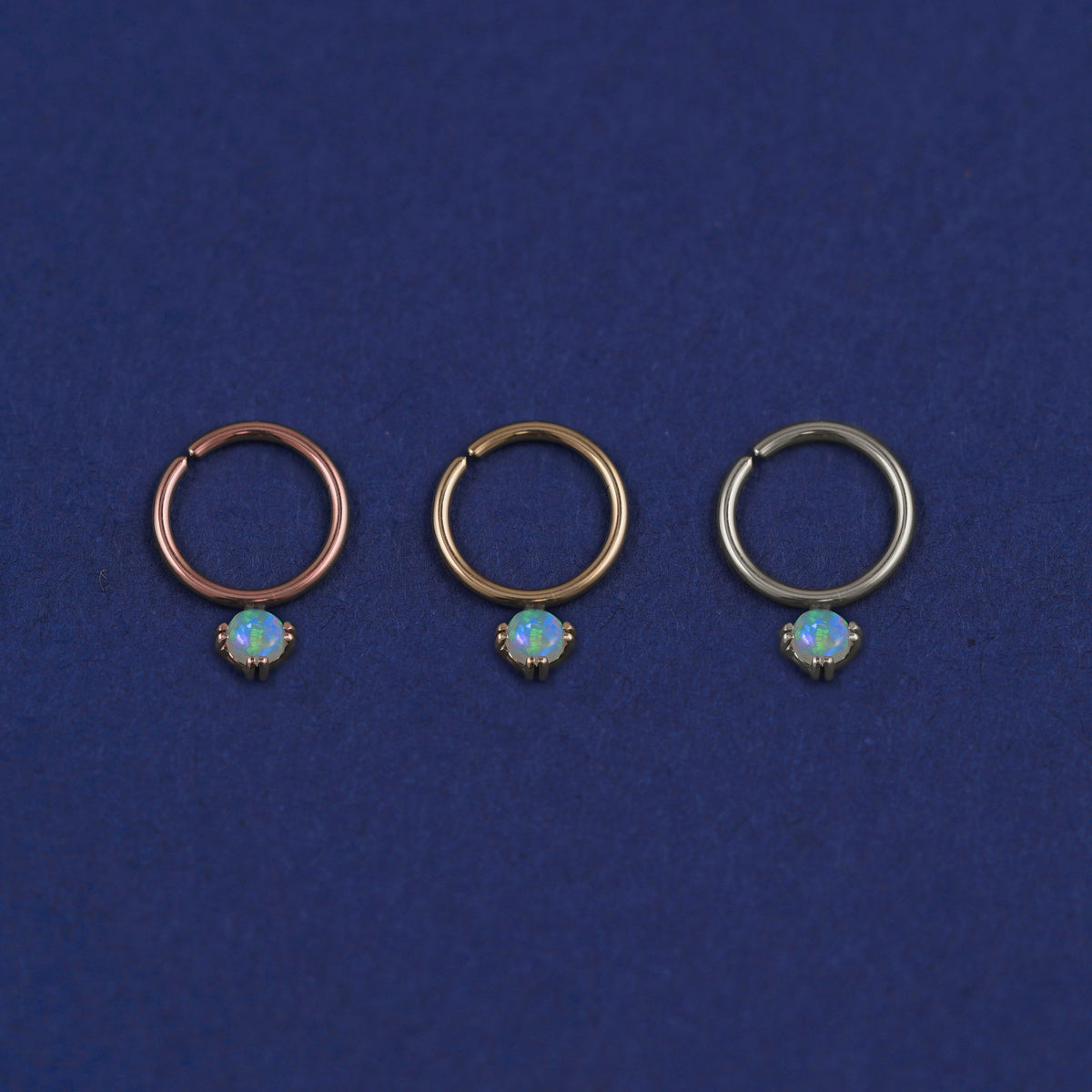 Three versions of the opal Pierced Gemstone Septum shown in options of rose, yellow, and white gold