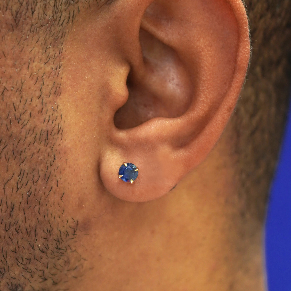 Close up view of a model's ear wearing a solid 14k gold blue sapphire pressure lock earring