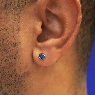 Close up view of a model's ear wearing a solid 14k gold blue sapphire pressure lock earring