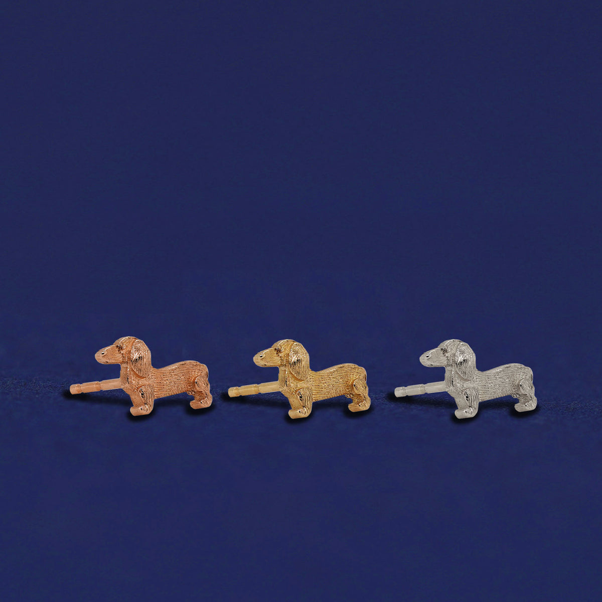 Three versions of the Dog Earrings shown in options of rose, yellow, and white gold