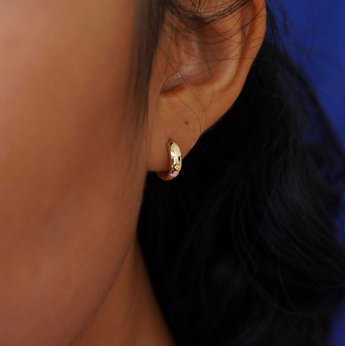 Close up view of a model's ear wearing a yellow gold Small Thick Huggie Hoop