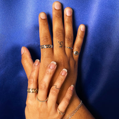 A model wearing yellow gold rings touching the wrist of a model wearing white gold rings