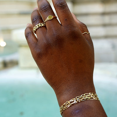 A raised hand in front of a building wearing a Signet Ring, a Wave Ring, and a Miami Cuban Ring