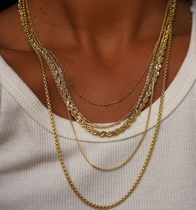 A model wearing a Beaded Essential, Rope, Figaro, Mini Miami, Thick Cable, Thick Rope, and Rounded Box Chains layered