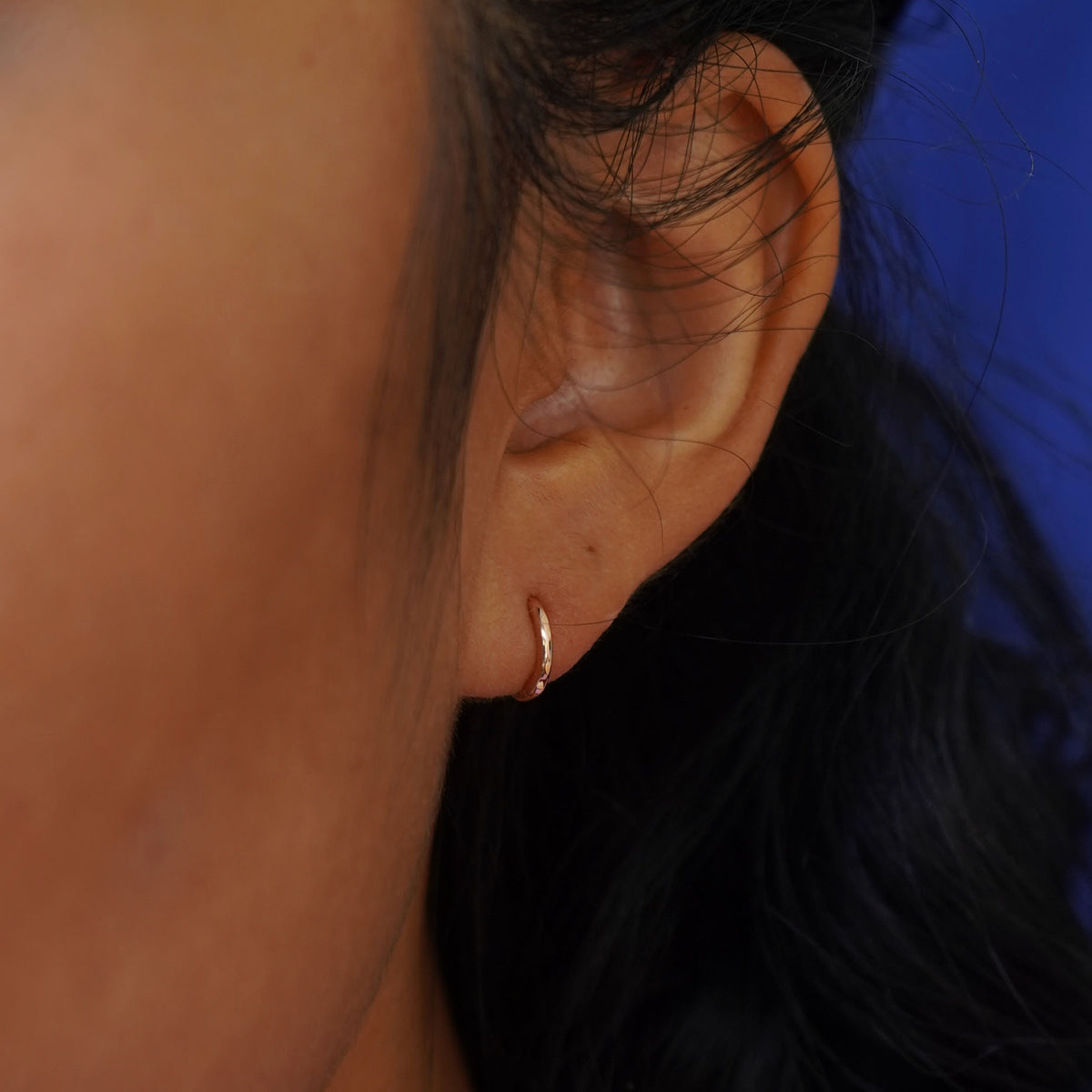 Close up view of a model's ear wearing a yellow gold Mini Curvy Huggie Hoop