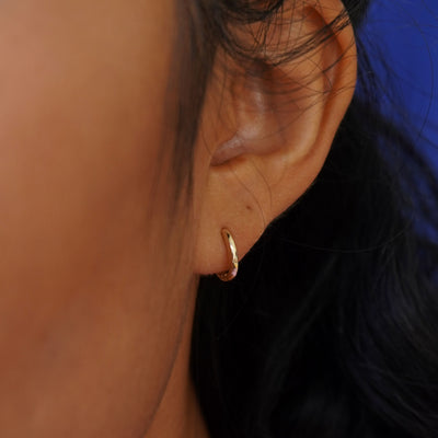 A model's ear wearing a 14k yellow gold Small Curvy Huggie Hoop